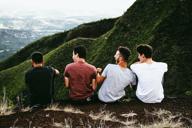 men sitting on cliff edge facing away from camera